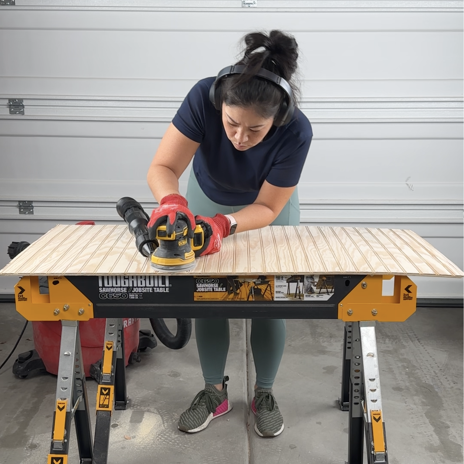 Deedee using an orbital sander on a sheet of beadboard in the garage